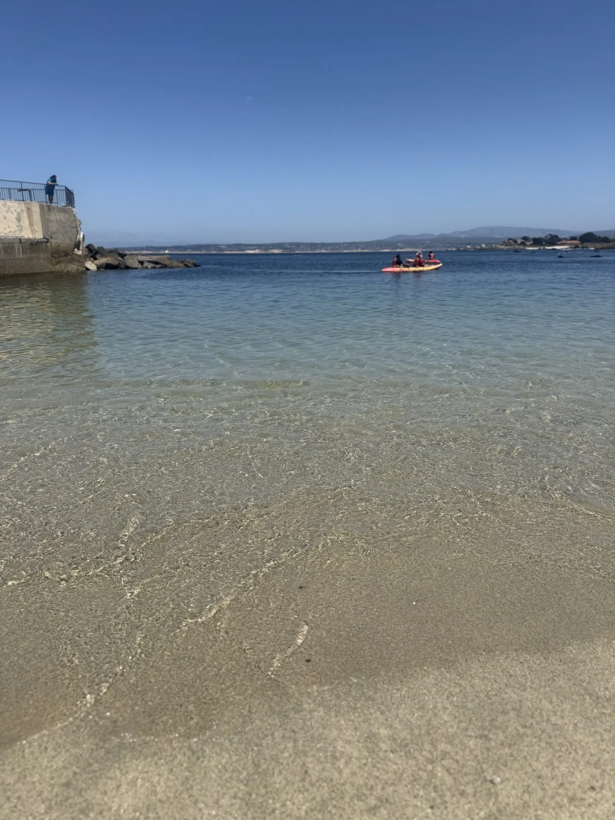 海水清澈见底，远处有人划着皮划艇往外海去