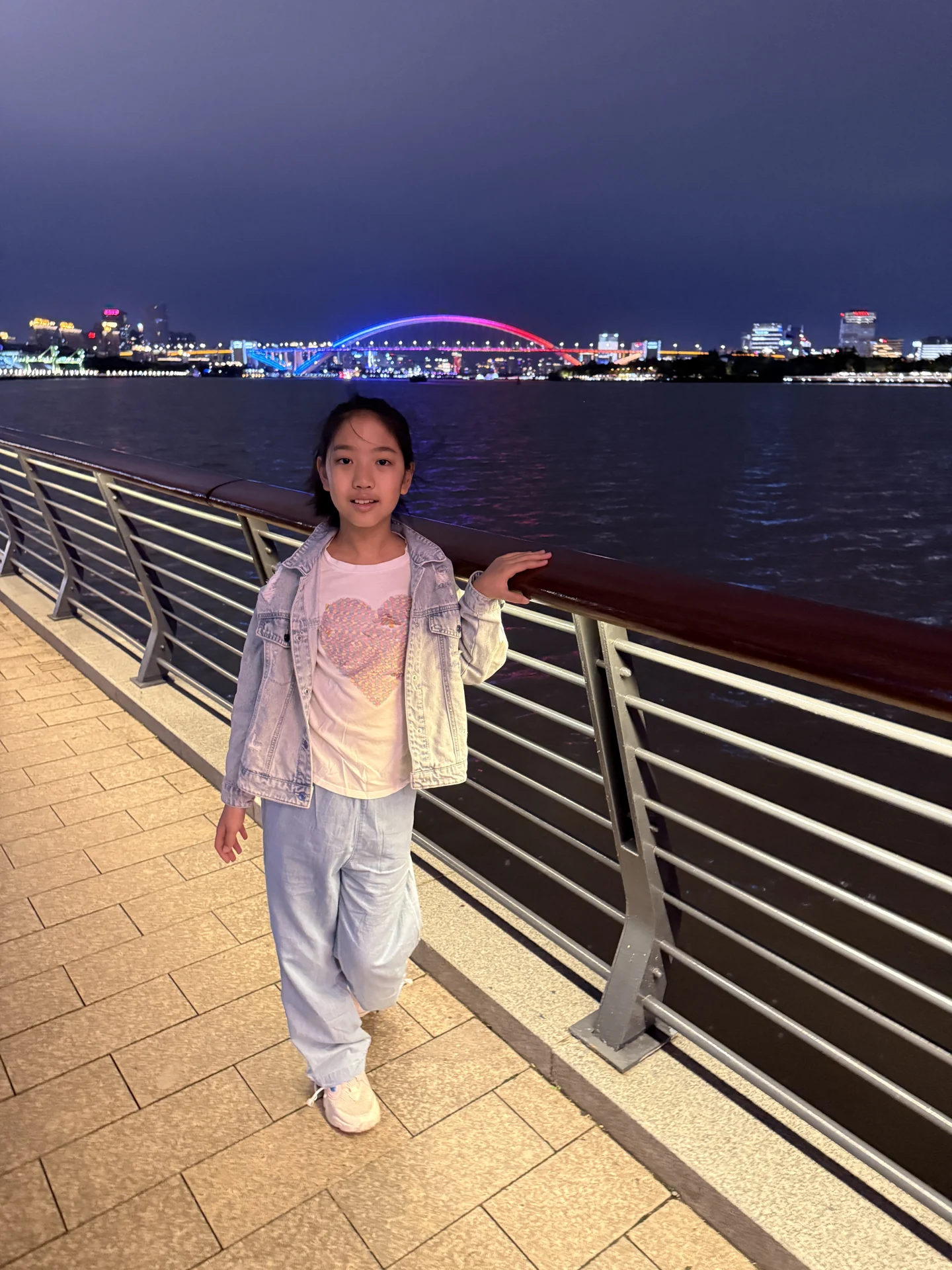 妹妹在江边抬起手掌,身后是大桥与夜色中的江面