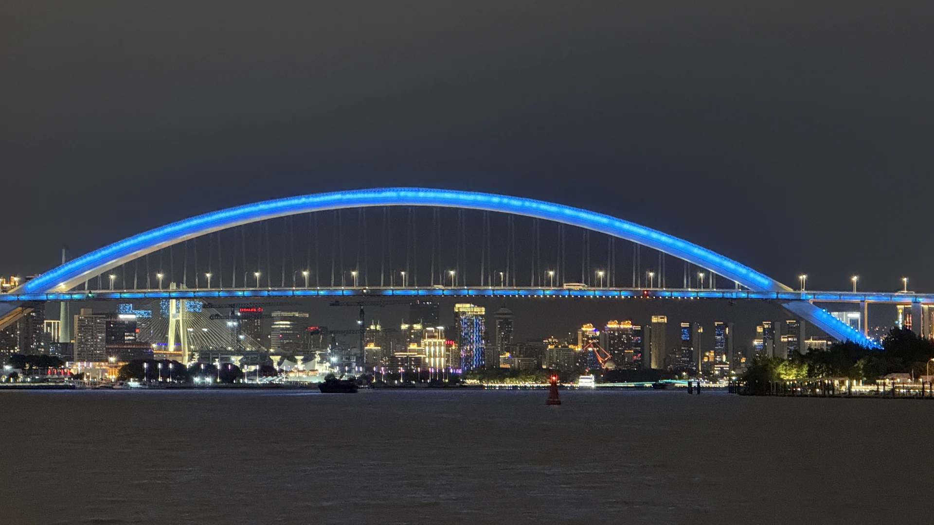 蓝色桥拱横跨黄浦江,两岸建筑灯光亮起